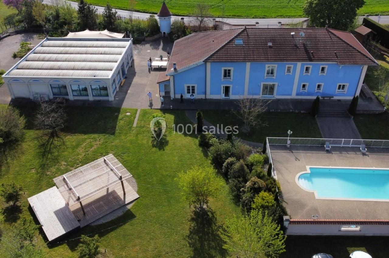 Vue aérienne d'une propriété avec maison bleue, piscine, pergola en bois et jardin verdoyant.