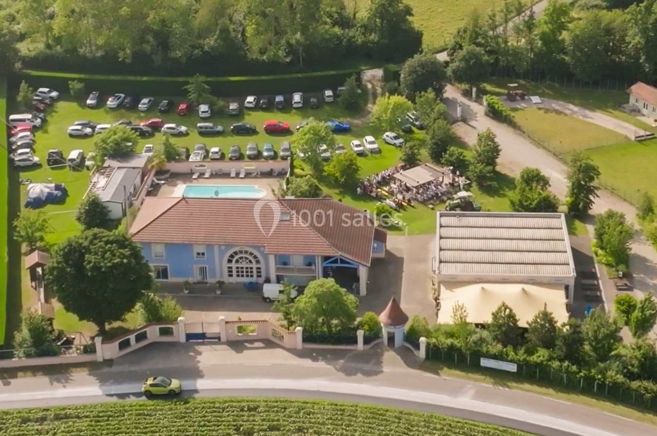 Vue aérienne d'un complexe avec piscine, parking, espaces verts et bâtiments entourés de champs et de routes.
