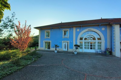 Espace extérieur couvert par une tente beige, avec des tables et des personnes assises dans un cadre verdoyant.