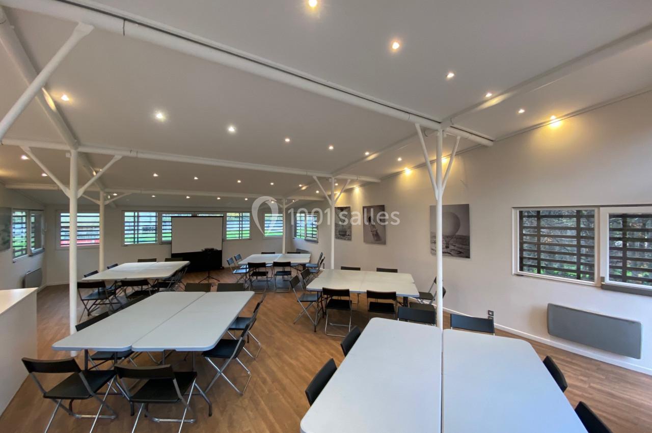 Salle lumineuse avec tables et chaises disposées pour une réunion ou un atelier, éclairée par des spots au plafond.