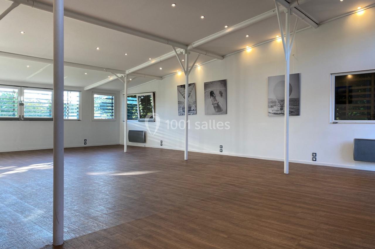 Salle lumineuse avec parquet en bois, murs blancs décorés de cadres, grandes fenêtres et éclairage encastré.