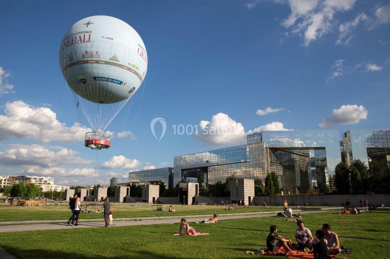 Montgolfière flottant au-dessus d'un parc verdoyant avec des personnes assises sur l'herbe par temps ensoleillé.