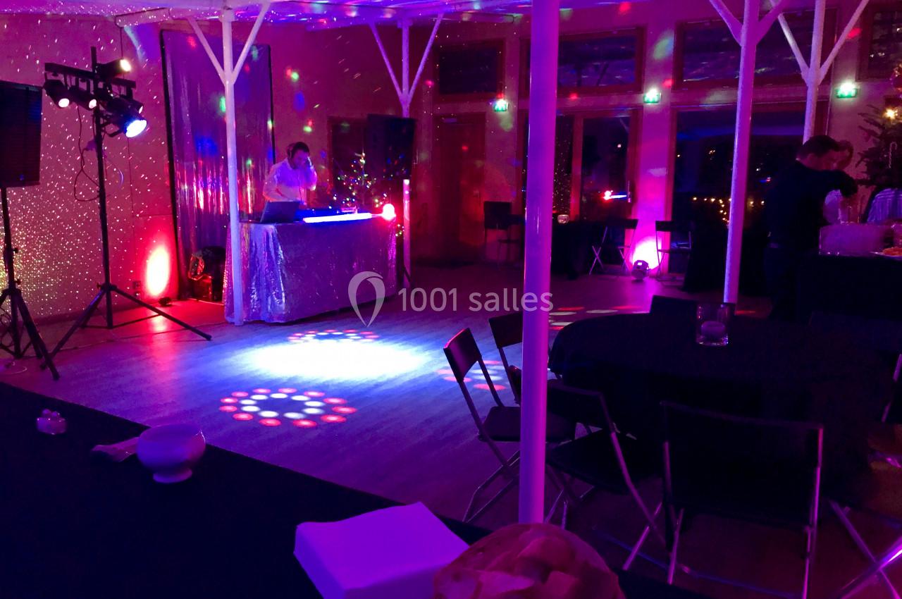 Salle de réception éclairée par des lumières colorées, avec une table de DJ et des tables dressées en arrière-plan.