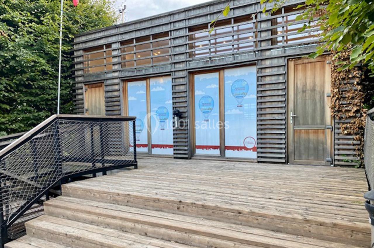 Façade en bois avec trois portes vitrées décorées de montgolfières, entourée de végétation et accessible par des marches en…