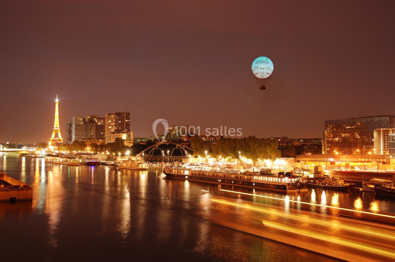 Vue nocturne de Paris avec la Seine, la tour Eiffel illuminée et un ballon captif dans le ciel.