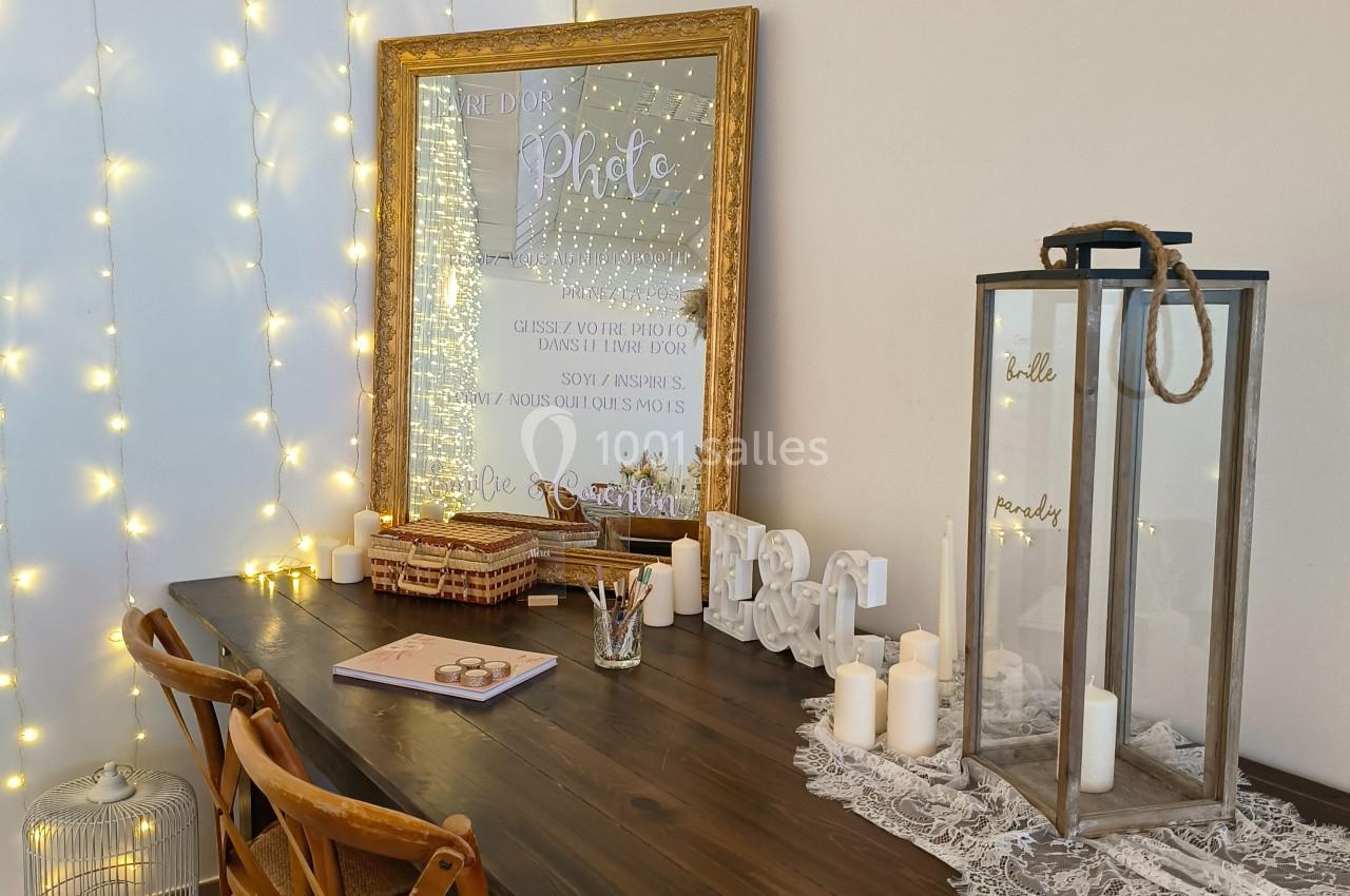 Table en bois décorée avec des bougies, une lanterne, un cadre lumineux et des guirlandes lumineuses accrochées au mur.