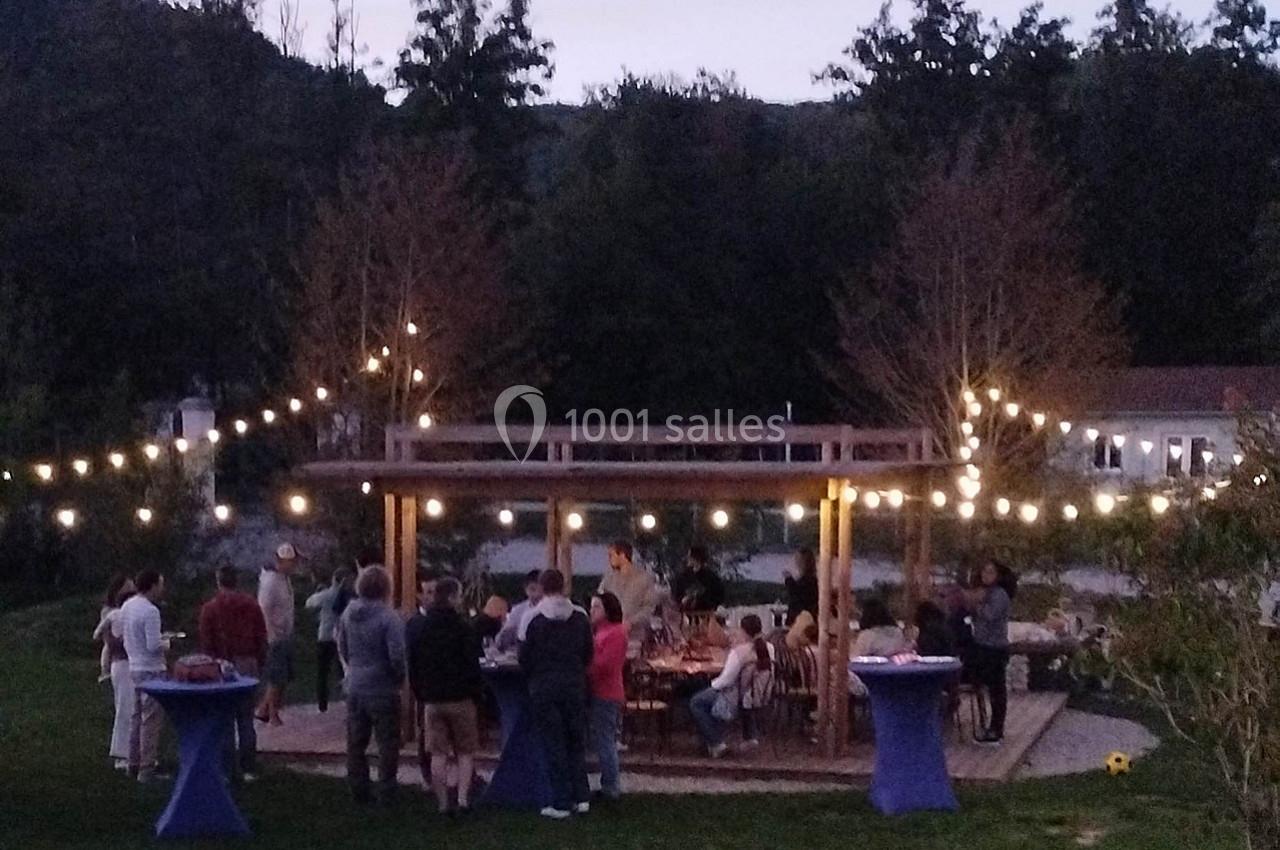 Des personnes rassemblées sous une pergola éclairée par des guirlandes lumineuses dans un jardin au crépuscule.