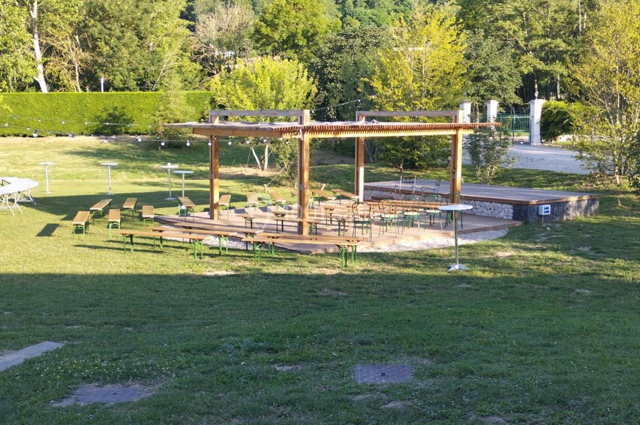 Structure en bois avec des bancs et des tables disposés en plein air sur une pelouse, entourée de verdure.