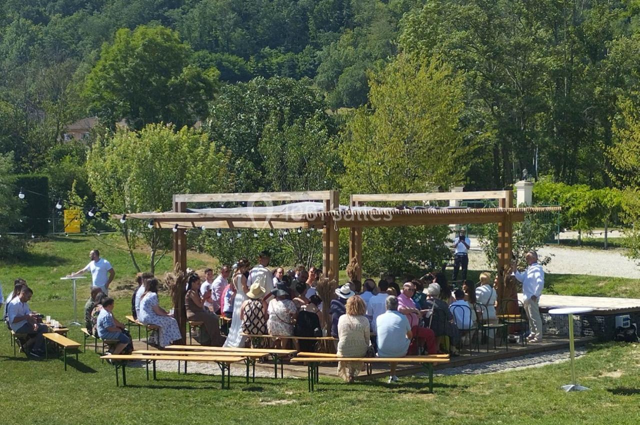 Groupe de personnes assises sous une pergola en bois dans un espace extérieur verdoyant par une journée ensoleillée.