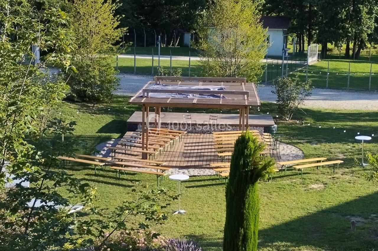 Vue d'un espace extérieur aménagé avec des bancs en bois et une pergola, entouré de verdure et d'arbres.