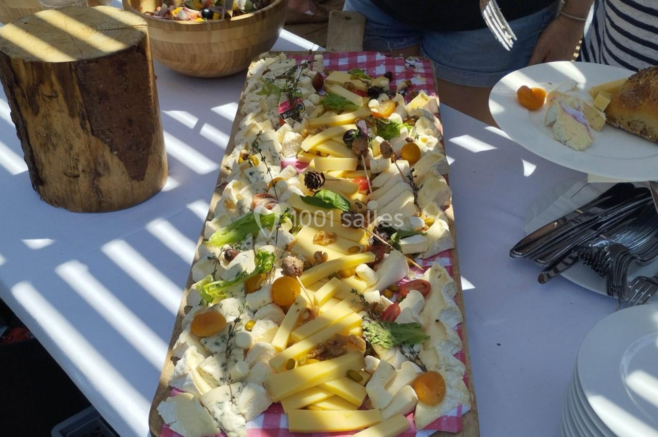 Plateau de fromages variés avec fruits secs et frais, présenté sur une planche en bois lors d'un buffet en extérieur.
