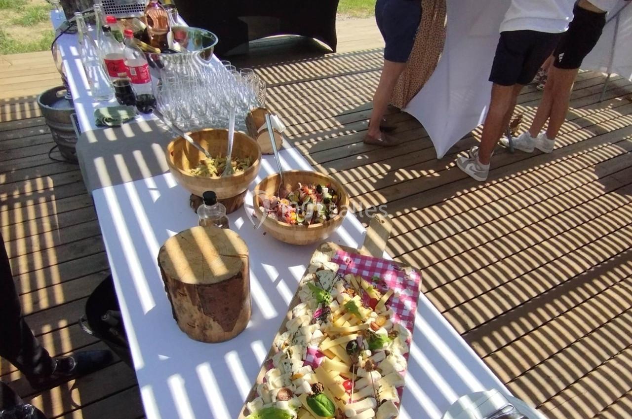 Table en extérieur avec buffet comprenant des boissons, des verres, des salades en bols et un plateau de fromages.