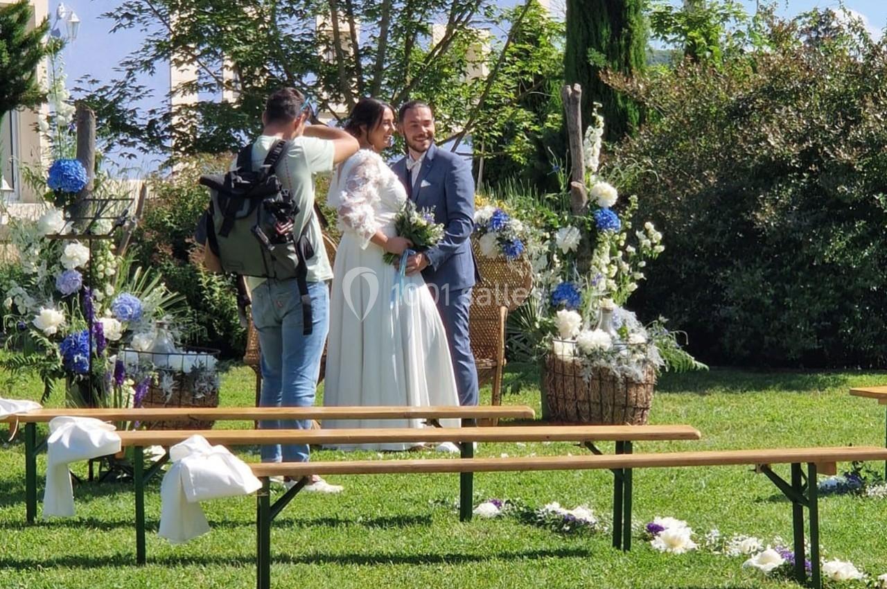Un photographe capture un couple de mariés souriants dans un jardin décoré de fleurs blanches et bleues.