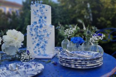Centre de table floral avec roses blanches, feuillage et bougies blanches, sur une table de réception décorée en bleu et…