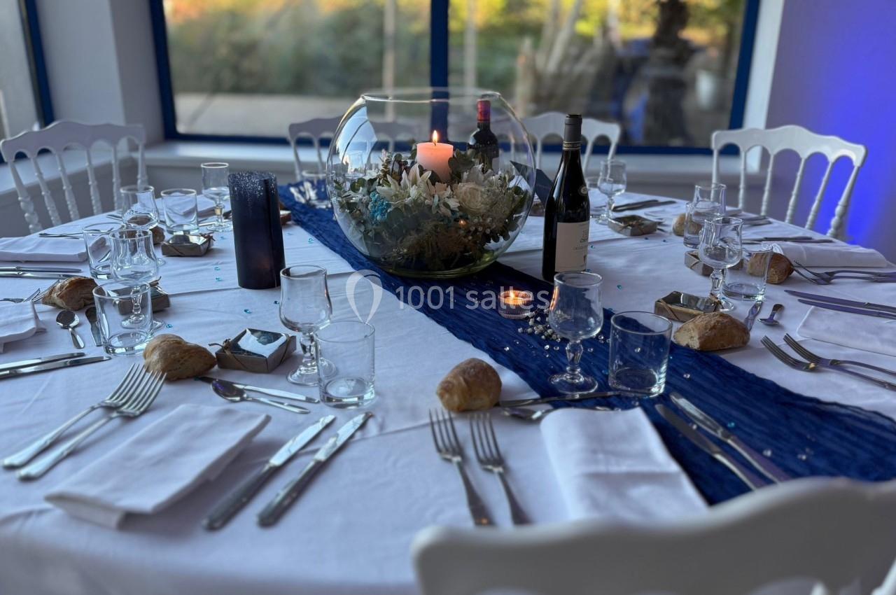 Table ronde dressée avec nappes blanches, décoration marine, verres, couverts, bougies et bouteilles de vin.