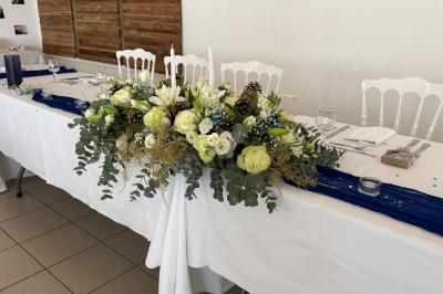 Centre de table floral avec roses blanches, feuillage et bougies blanches, sur une table de réception décorée en bleu et…