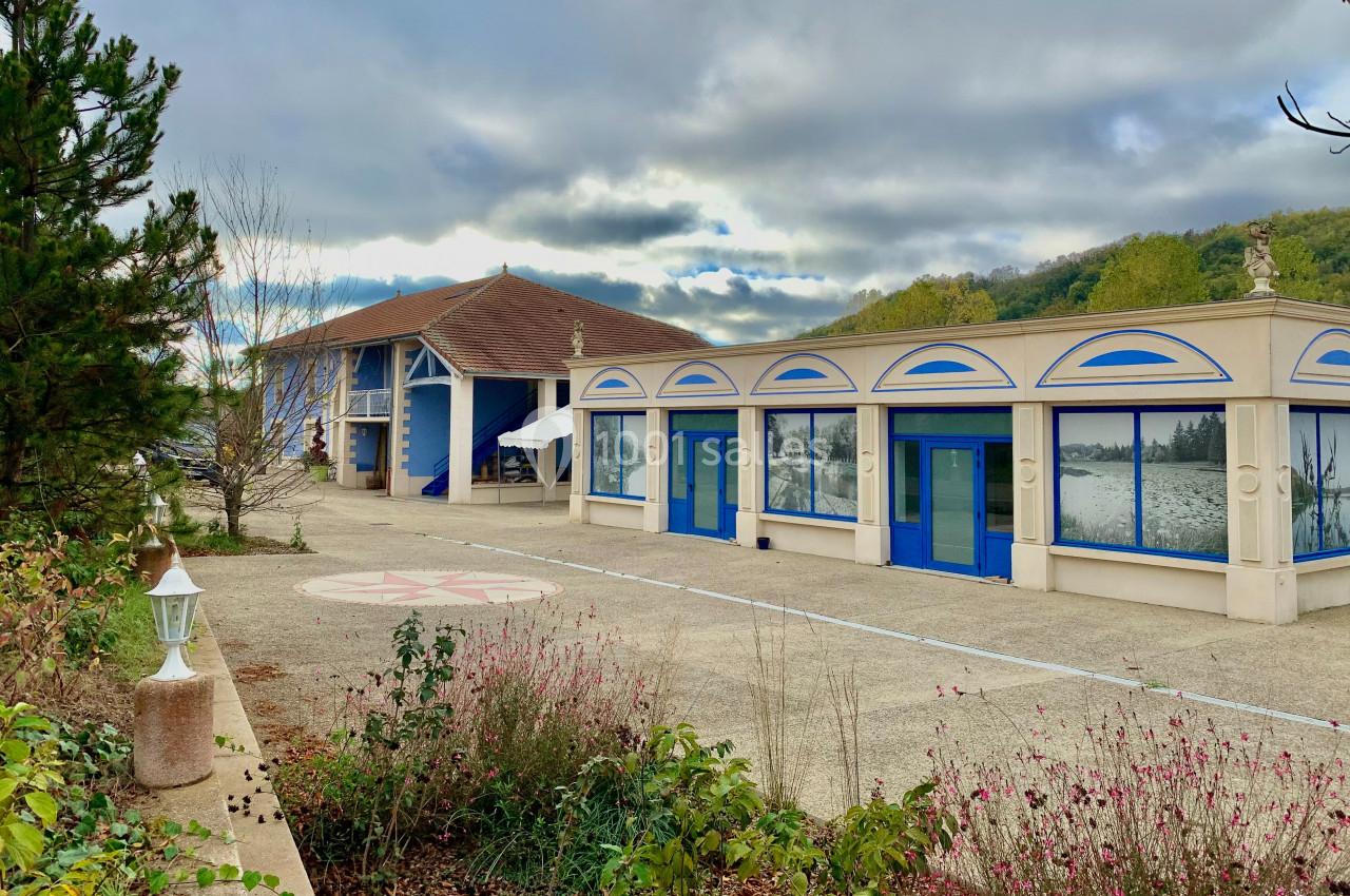 Bâtiment avec façade bleue et beige, entouré de végétation, sous un ciel nuageux.