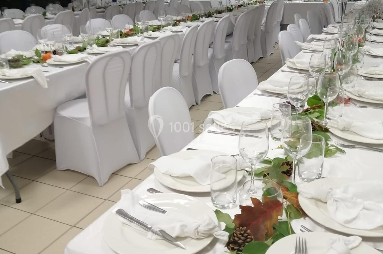 Tables de réception alignées, décorées de nappes blanches, vaisselle élégante et ornements végétaux.
