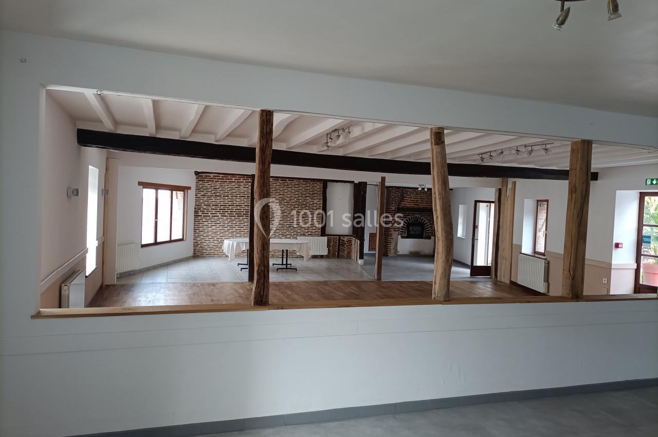 Salle spacieuse avec murs en briques, poutres apparentes et grandes fenêtres laissant entrer la lumière naturelle.