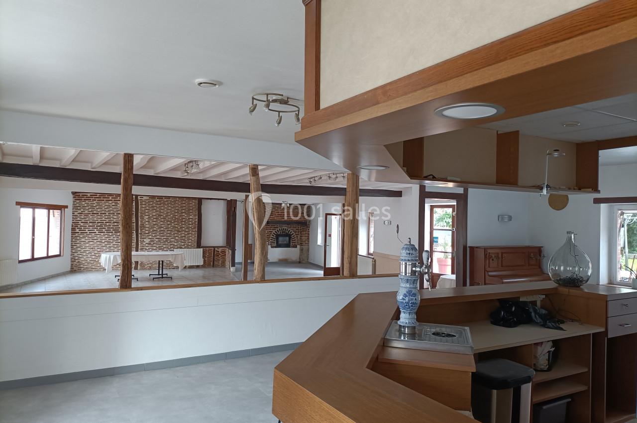 Intérieur d'une maison avec un comptoir en bois au premier plan et une grande pièce avec murs en briques au fond.