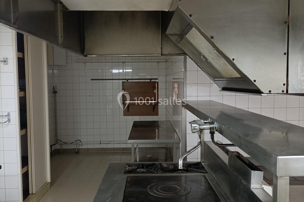 Cuisine professionnelle avec plaques de cuisson, hotte en métal et murs carrelés blancs, espace dégagé et fonctionnel.