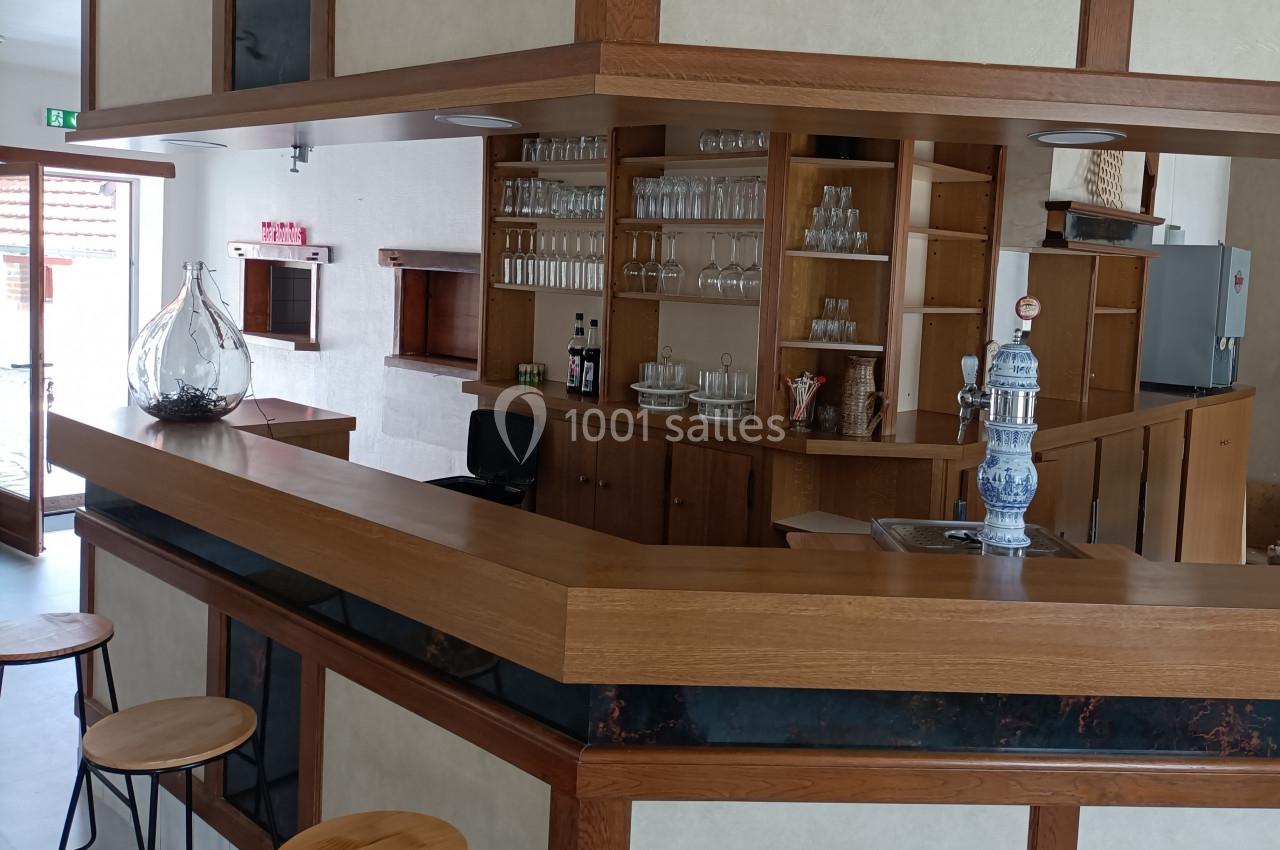 Comptoir en bois d'un bar avec tabourets hauts, étagères garnies de verres et une tireuse à bière.