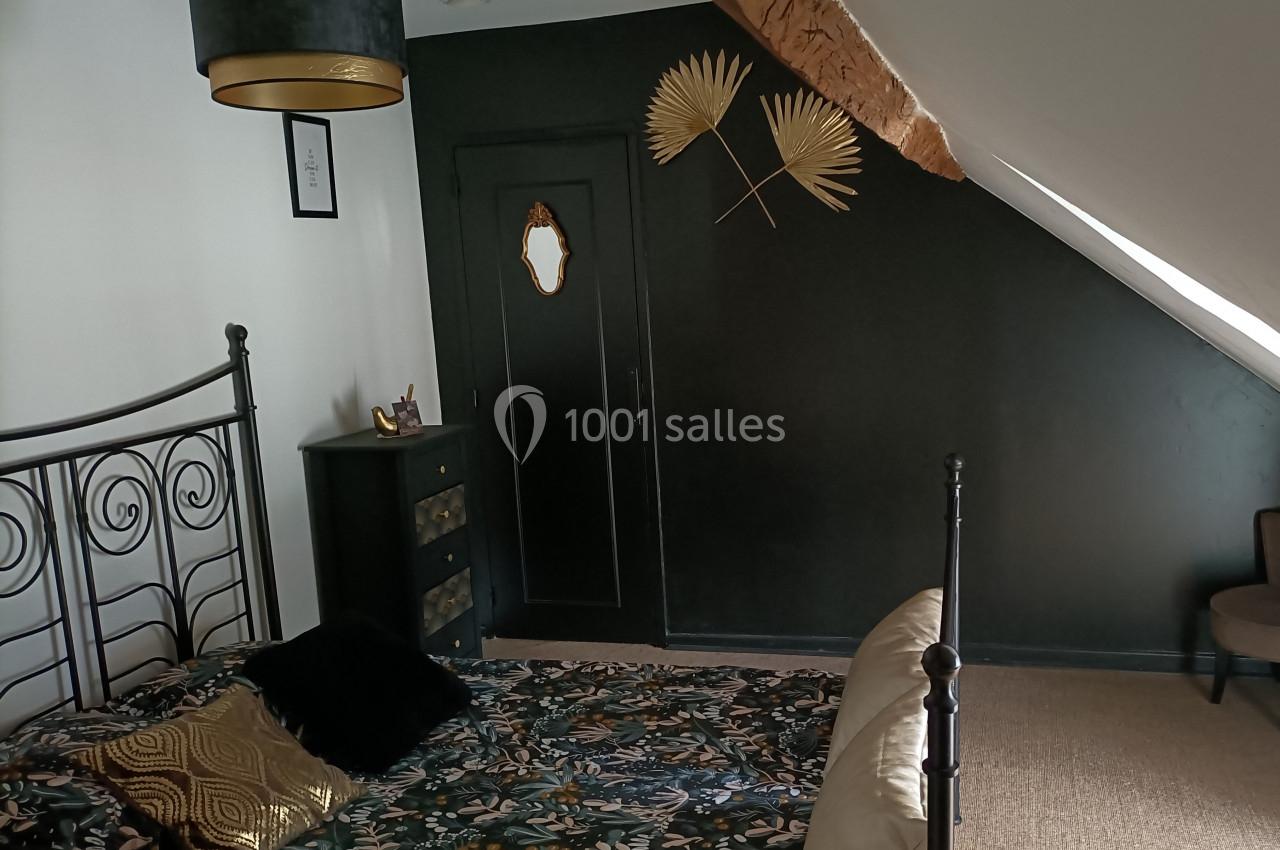 Chambre mansardée avec un mur noir décoré de feuilles dorées, un lit en métal et une commode assortie.