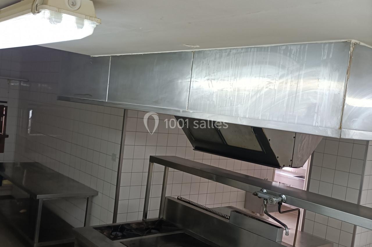 Cuisine professionnelle avec plaques de cuisson, hotte en inox, carrelage mural blanc et éclairage fluorescent.