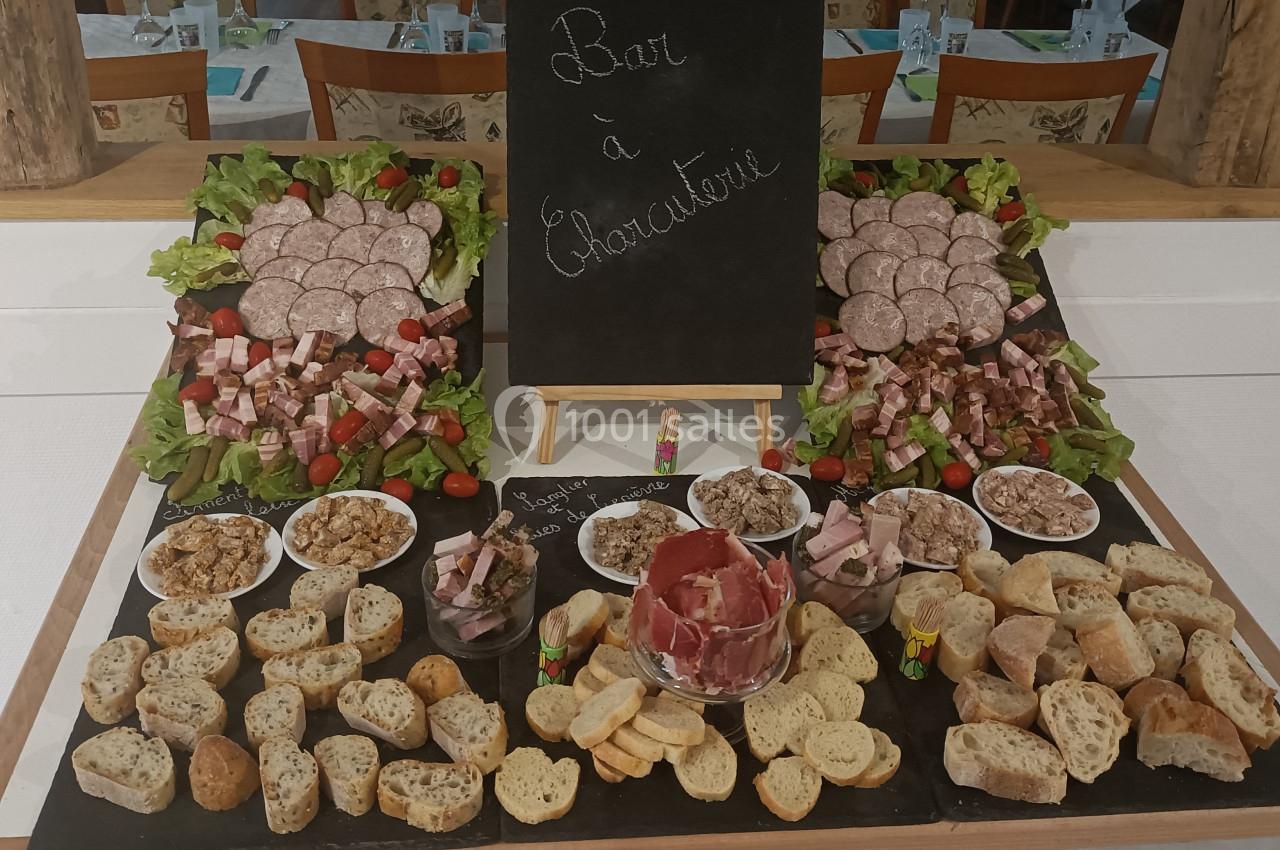 Plateau de charcuterie avec saucissons, pâtés, jambons, pain et garnitures disposés autour d'un tableau noir.