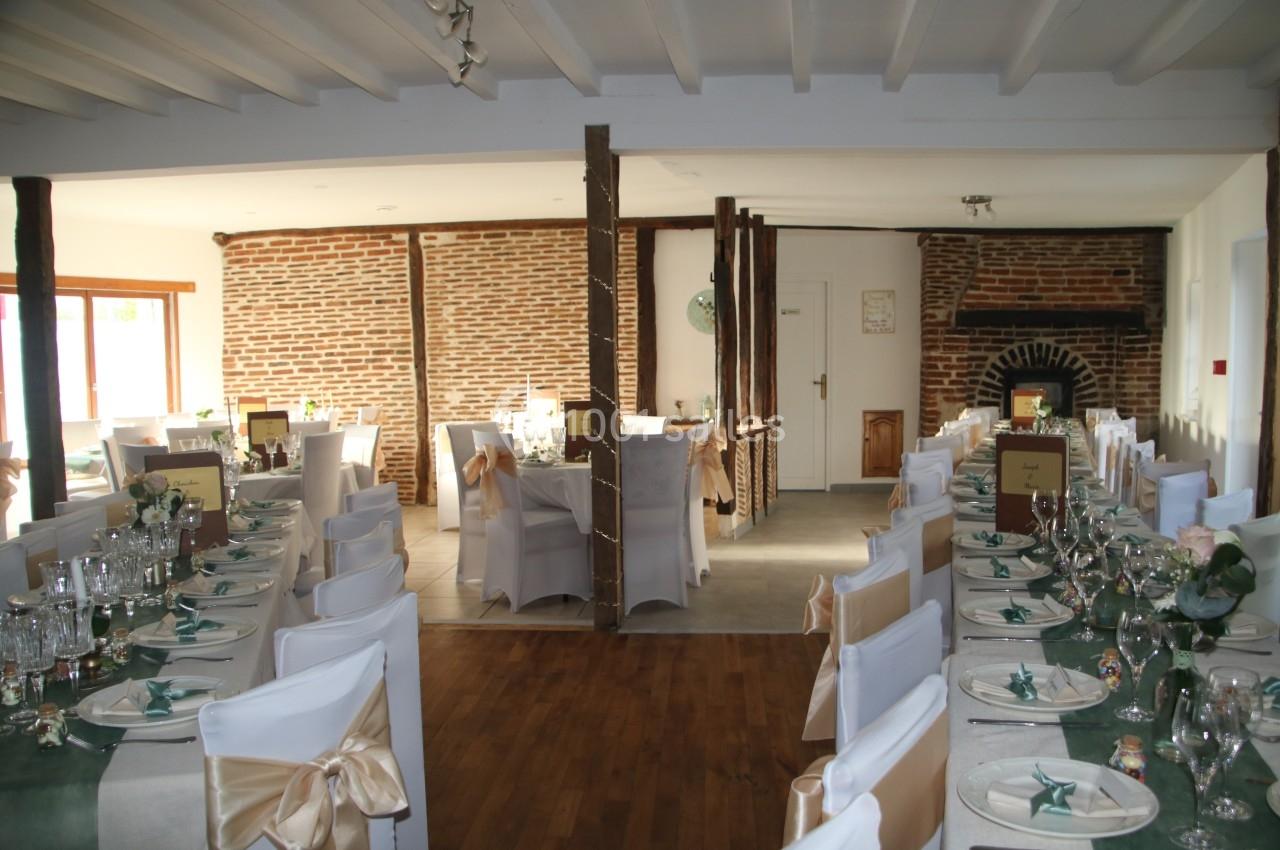 Salle de réception décorée avec des tables dressées, chaises blanches et murs en briques apparentes.