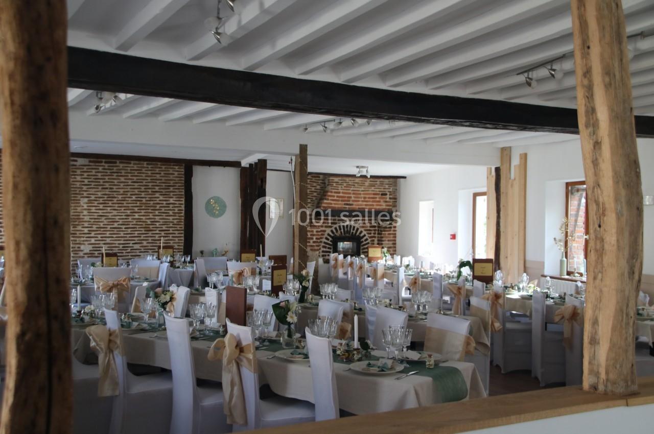 Salle de réception décorée avec des tables dressées, des chaises blanches et des éléments rustiques en bois et briques.