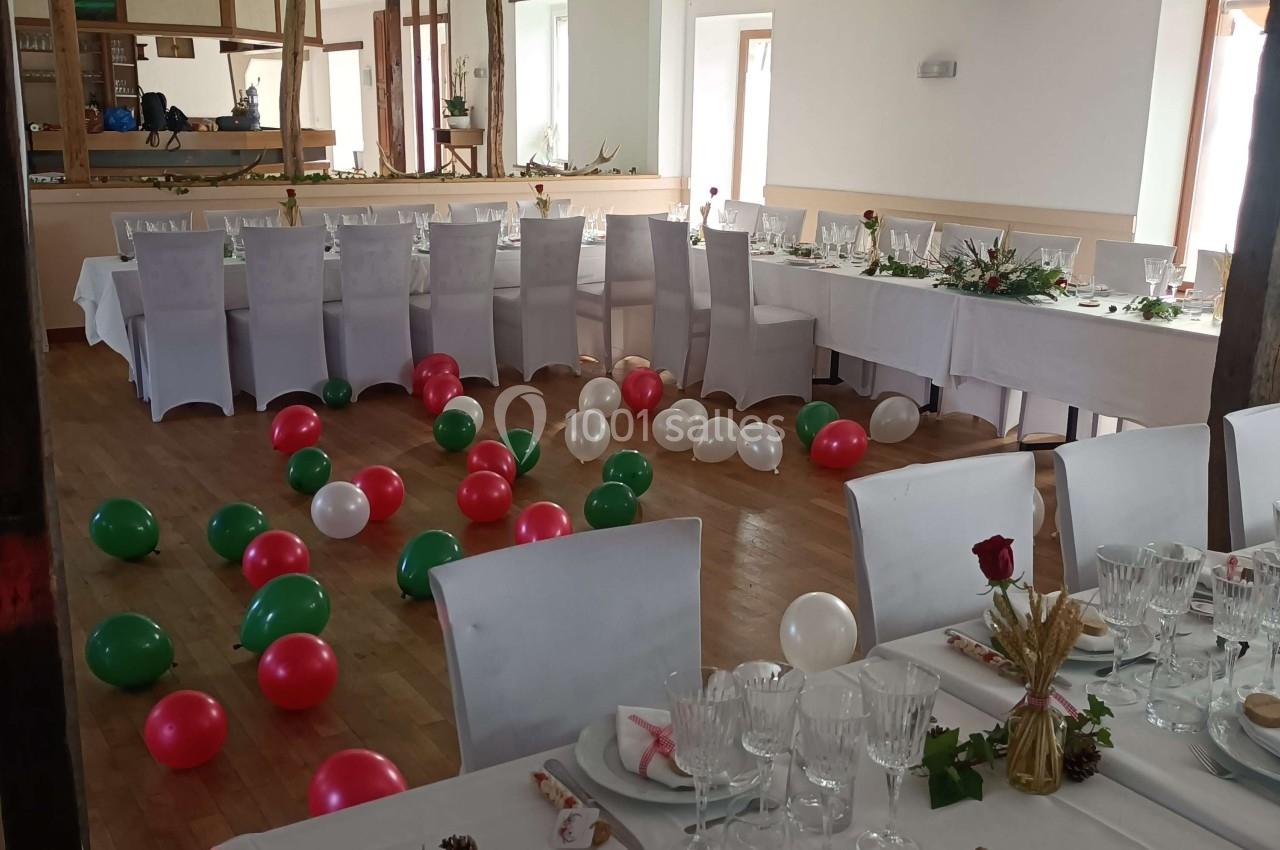 Salle décorée pour un événement avec tables dressées, ballons colorés au sol et éléments végétaux en centre de table.