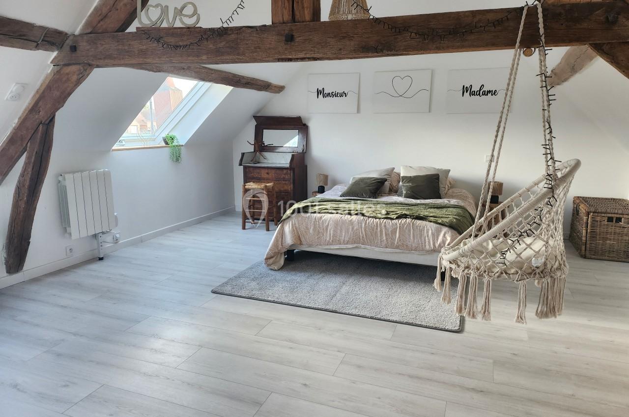 Chambre lumineuse sous combles avec poutres apparentes, lit double, fauteuil suspendu et bureau en bois.