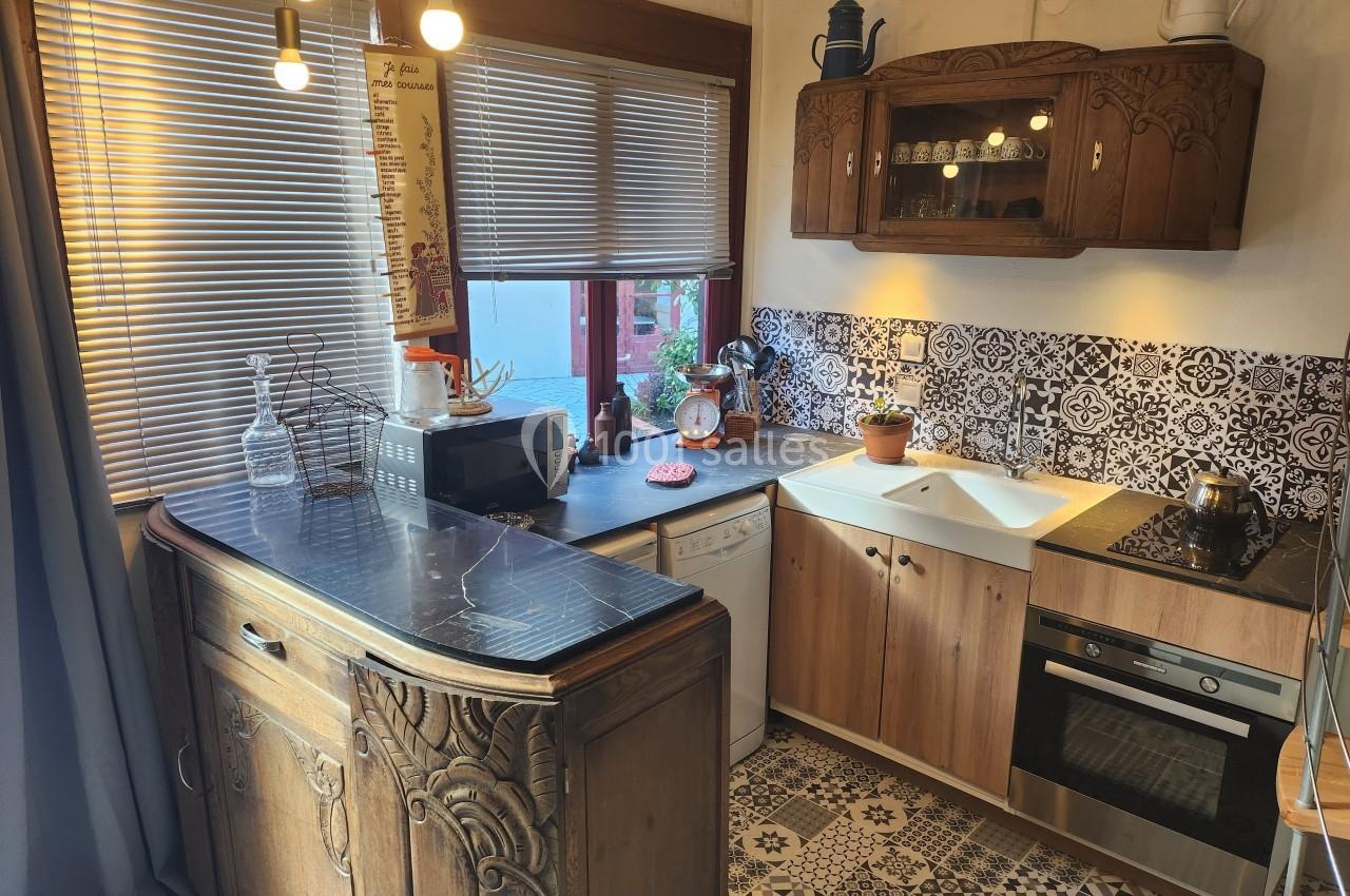 Cuisine rustique avec meubles en bois sculpté, plan de travail sombre, électroménagers modernes et carrelage décoratif.