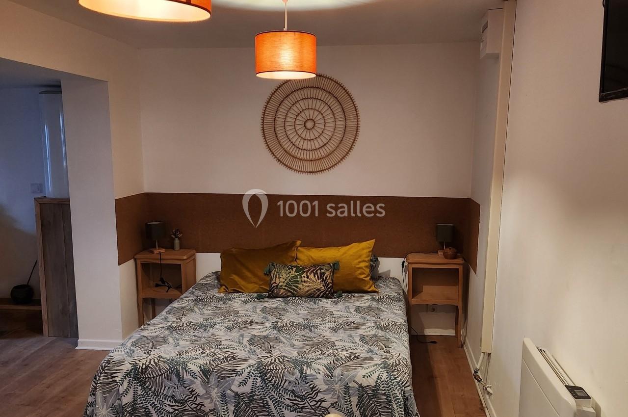 Chambre avec lit double, linge à motifs végétaux, coussins colorés, décor mural en rotin et éclairage suspendu.