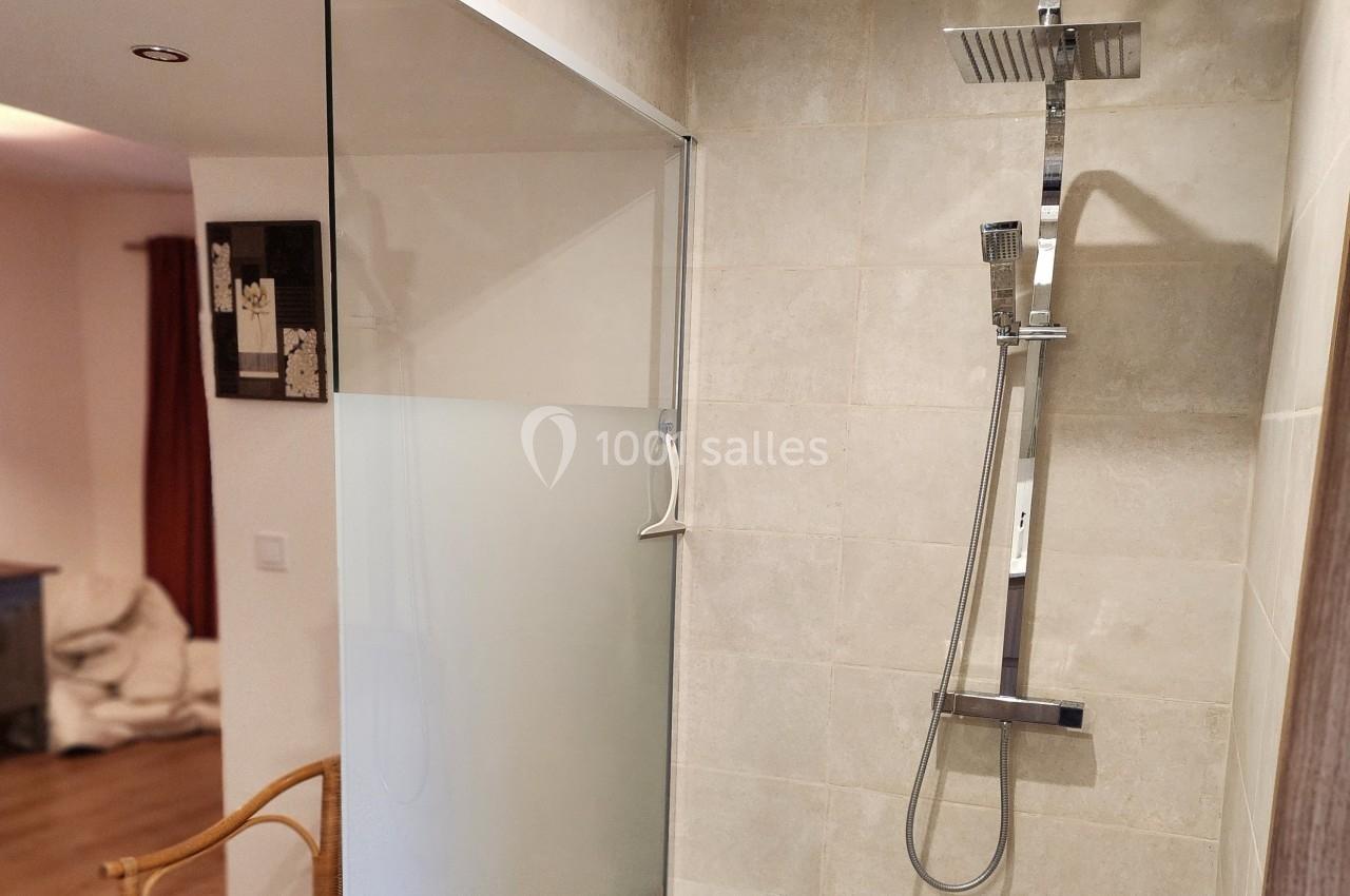 Douche moderne avec paroi vitrée et carrelage beige, équipée d'une colonne de douche chromée avec pommeau et douchette.