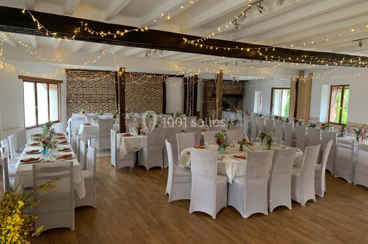 Salle de réception décorée avec des guirlandes lumineuses, tables dressées avec nappes blanches et chaises assorties.