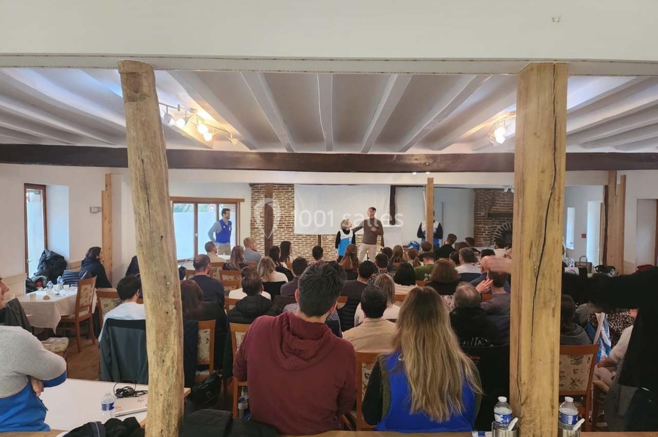 Un groupe de personnes assiste à une présentation dans une salle avec des poutres en bois et un mur en briques.