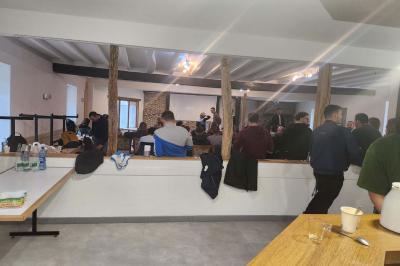 Un groupe de personnes assises et debout dans une salle avec des poutres apparentes, participant à une présentation.