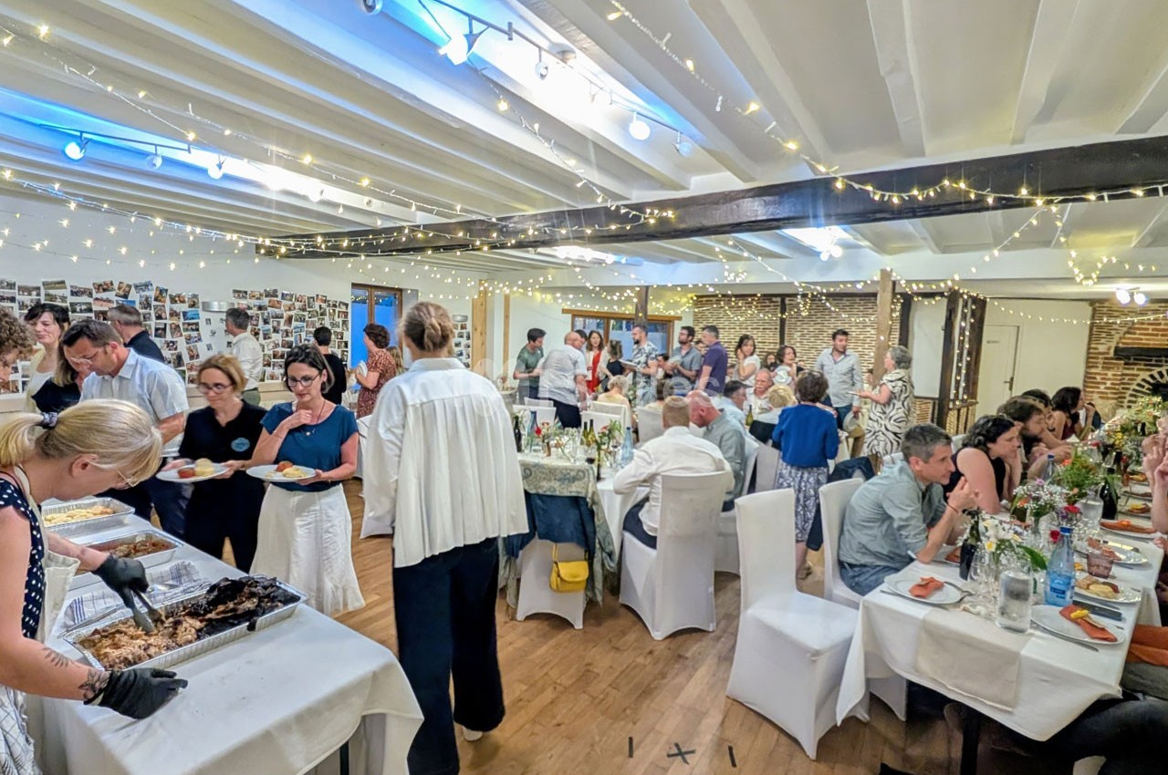 Salle décorée pour un événement avec des invités se servant à un buffet et discutant autour de tables dressées.