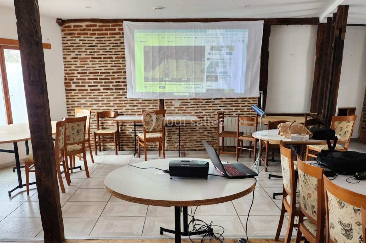 Salle avec des tables et des chaises en bois, un projecteur affichant une image sur un mur en briques.