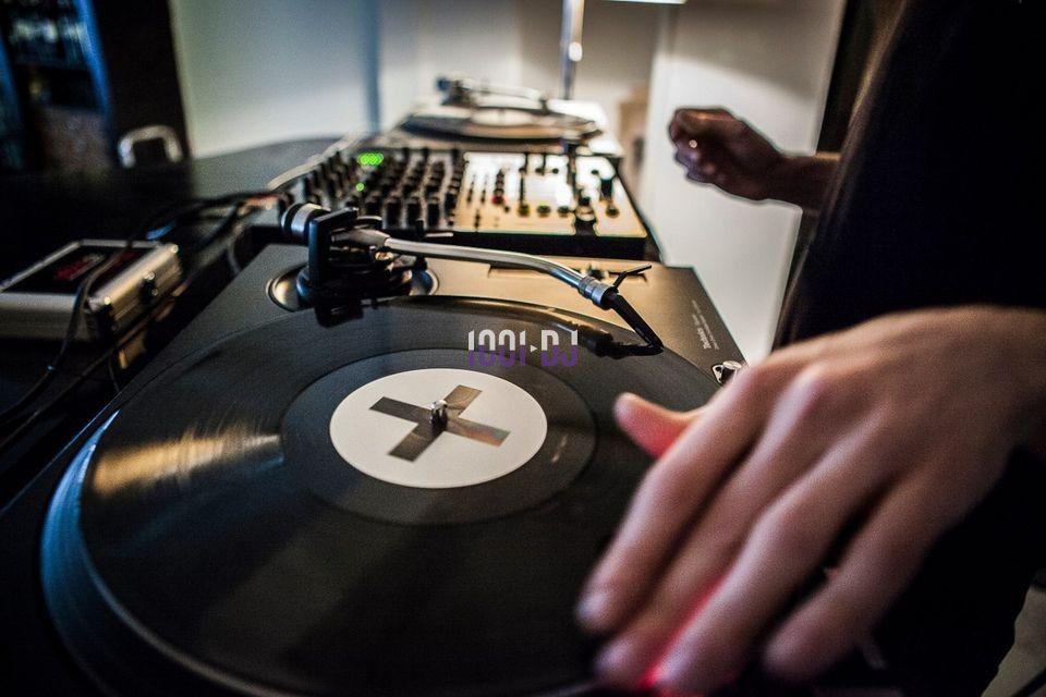 Un DJ manipule un disque vinyle sur une platine, avec une table de mixage en arrière-plan.