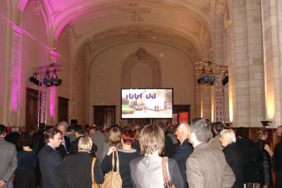 Entrée d'un bâtiment en briques avec porte ouverte, escaliers, pots de fleurs et haut-parleurs disposés de chaque côté.