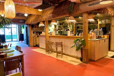 Comptoir en bois d'un bar à thème tropical avec tabourets pliants, éclairage en paille et décoration végétale.