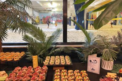 Comptoir en bois d'un bar à thème tropical avec tabourets pliants, éclairage en paille et décoration végétale.