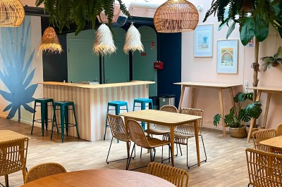 Comptoir en bois d'un bar à thème tropical avec tabourets pliants, éclairage en paille et décoration végétale.