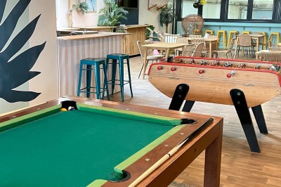 Comptoir en bois d'un bar à thème tropical avec tabourets pliants, éclairage en paille et décoration végétale.