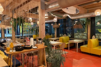 Comptoir en bois d'un bar à thème tropical avec tabourets pliants, éclairage en paille et décoration végétale.