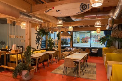 Comptoir en bois d'un bar à thème tropical avec tabourets pliants, éclairage en paille et décoration végétale.