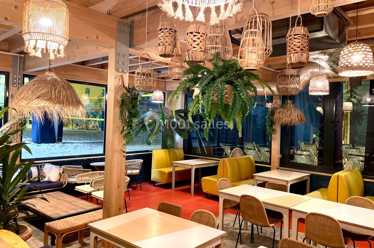 Salle lumineuse avec décoration tropicale, mobilier en bois et rotin, plantes suspendues et luminaires variés.